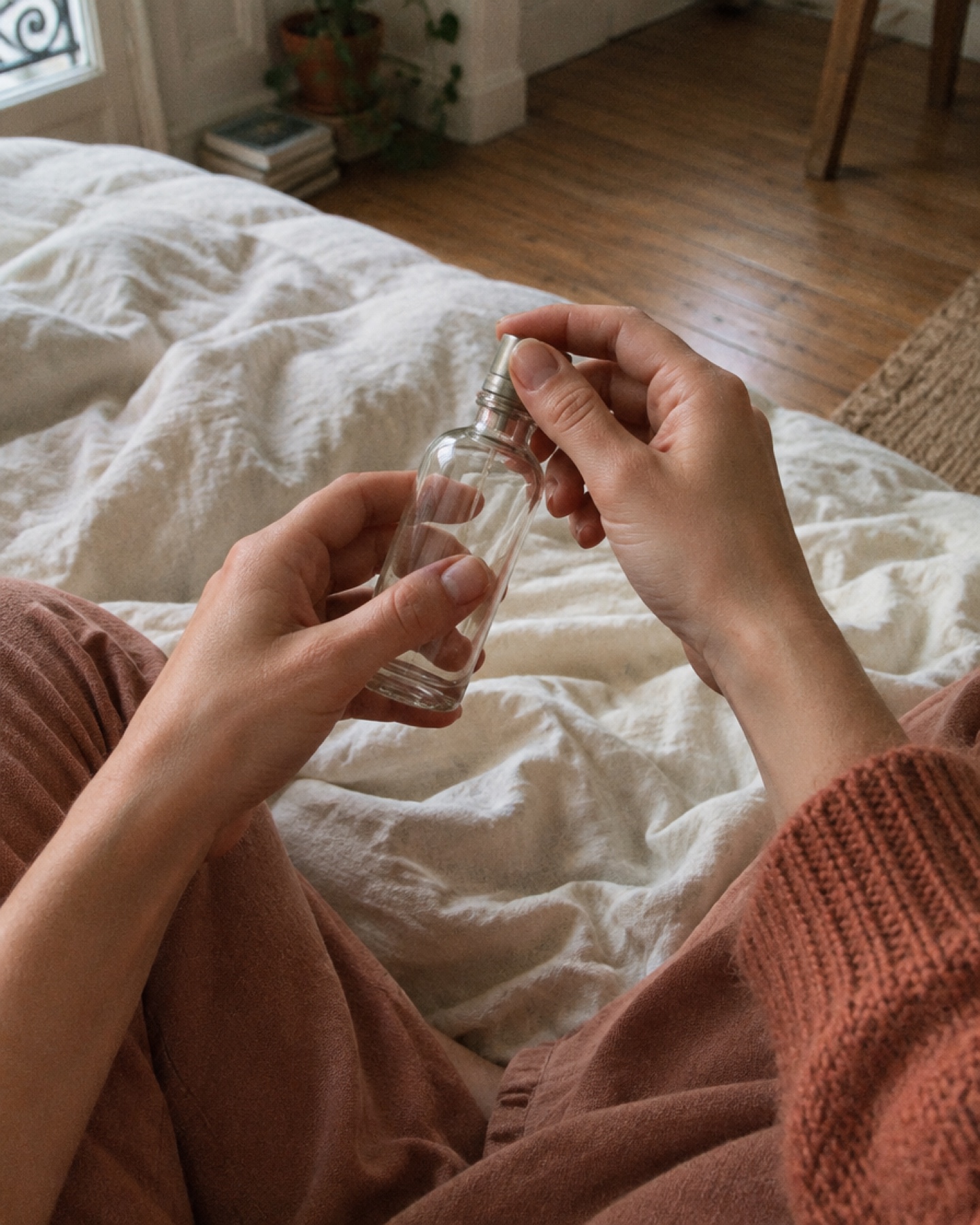 Mains tournant un petit flacon de verre, assise sur des draps froissés