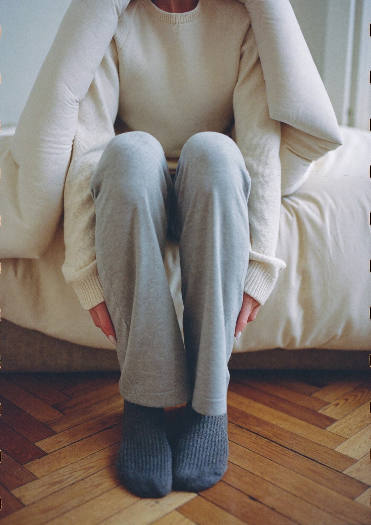 Assise au bord du lit, genoux repliés, enveloppée dans la couette