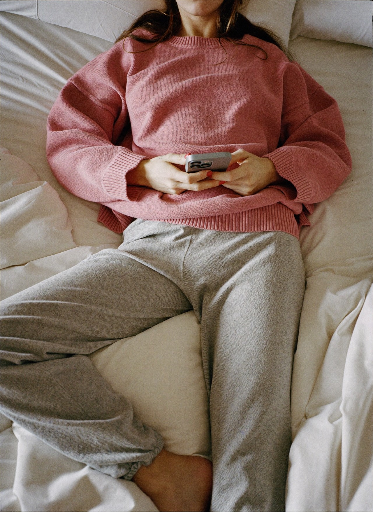 Vue de dessus, mains tenant un téléphone sur des draps froissés